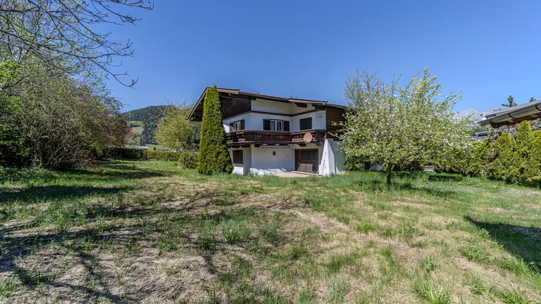 Haus im alpinen Stil mit großem Gartenbereich und Balkon unter blauem Himmel.