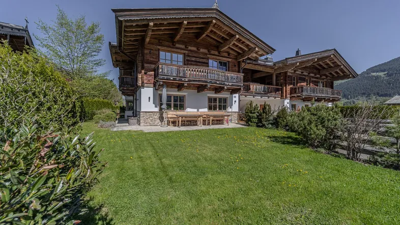 Traditionelles Holzchalet mit großem Garten und Bergblick unter blauem Himmel.