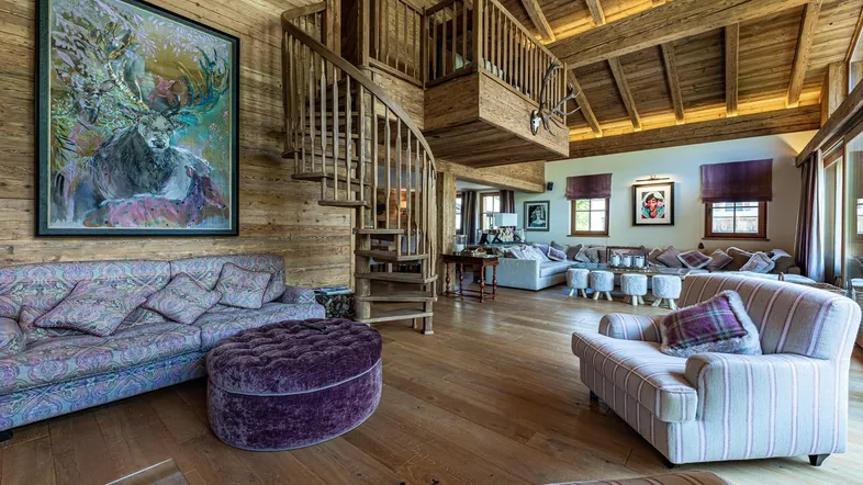 Geräumiges Wohnzimmer mit hohen Holzdecken, Wendeltreppe, großem Sofa und alpiner Kunst.