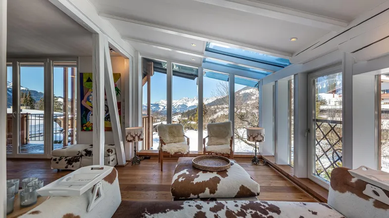 Helles Wohnzimmer mit großen Fenstern, Bergblick und gemütlichen Möbeln im alpinen Stil.