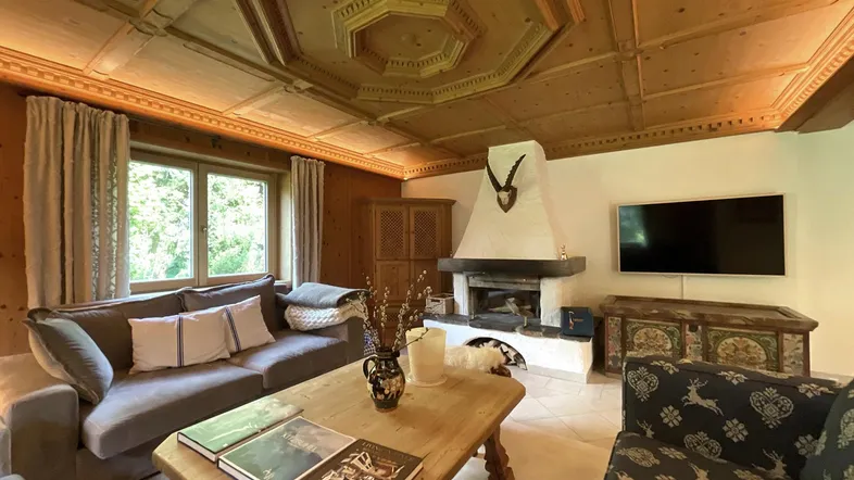 Gemütliches Wohnzimmer im alpinen Stil mit Holztäfelung, Kamin und traditioneller Deckenverzierung.