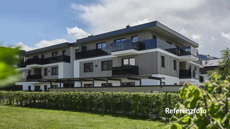 Modernes Mehrfamilienhaus mit Holzfassade und Balkonen, umgeben von Grünflächen unter blauem Himmel.
