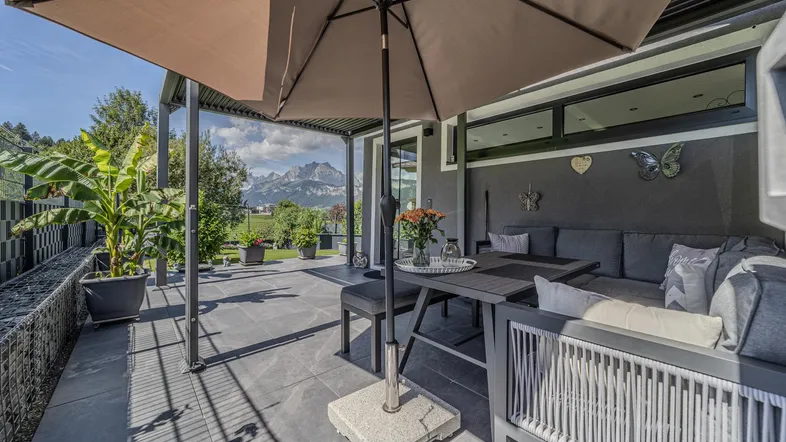Geräumige Terrasse mit bequemen Loungemöbeln, Sonnenschirm und beeindruckendem Bergblick.