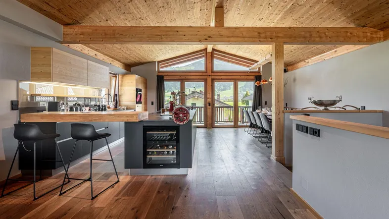 Offener Wohn- und Essbereich mit moderner Küche, Holzbalkendecke und Bergblick durch große Fenster.
