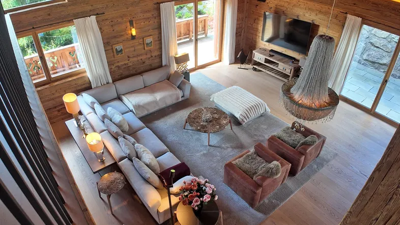 Geräumiges Wohnzimmer im alpinen Stil mit Holzwänden, hohen Decken und Zugang zu einem Balkon.