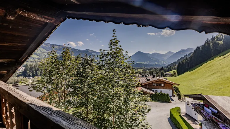 Blick von einem rustikalen Holzbalkon auf die umliegende Berglandschaft und ein charmantes Dorf.