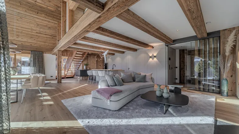 Geräumiger offener Wohnbereich mit Holzbalken, modernem Sofa und Blick auf den Essbereich.