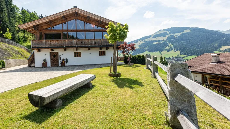 Traditionelles Holzhaus mit weißer Fassade und Bergblick in grüner Umgebung.