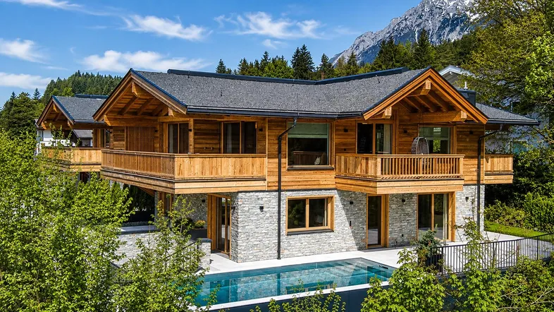 Modernes Chalet mit Holz- und Steinfassade, Balkonen, Infinity-Pool und Bergblick in alpiner Umgebung.