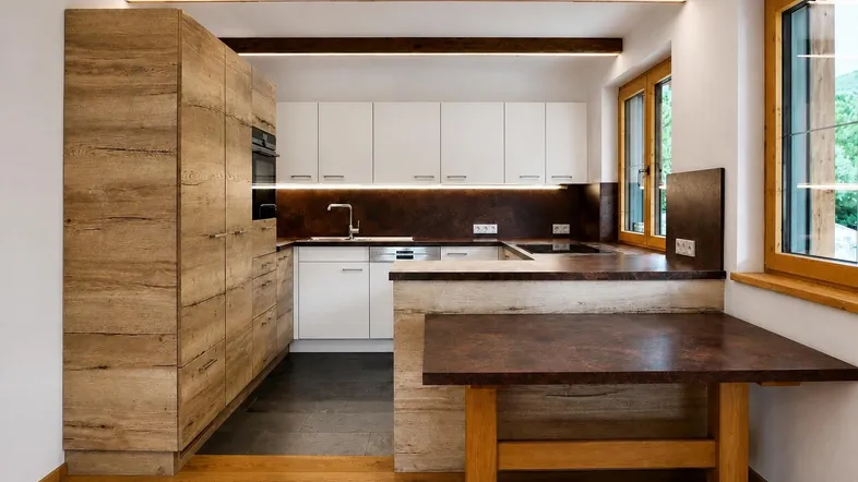Moderne Küche mit Holzelementen, weißen Schränken und dunkler Arbeitsplatte, gut beleuchtet durch integrierte Lichter.