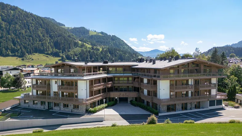 Modernes Mehrfamilienhaus in alpiner Umgebung mit Holzbalkonen und Bergblick.