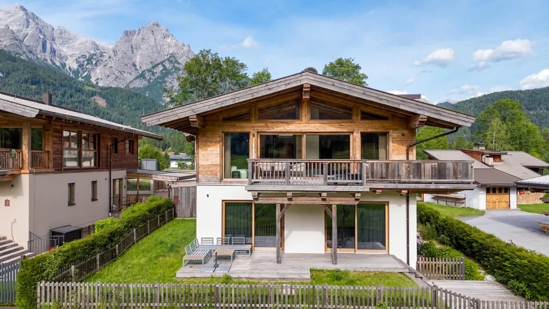 Modernes Chalet mit Holzfassade, großen Fenstern und Balkon vor beeindruckender Bergkulisse.
