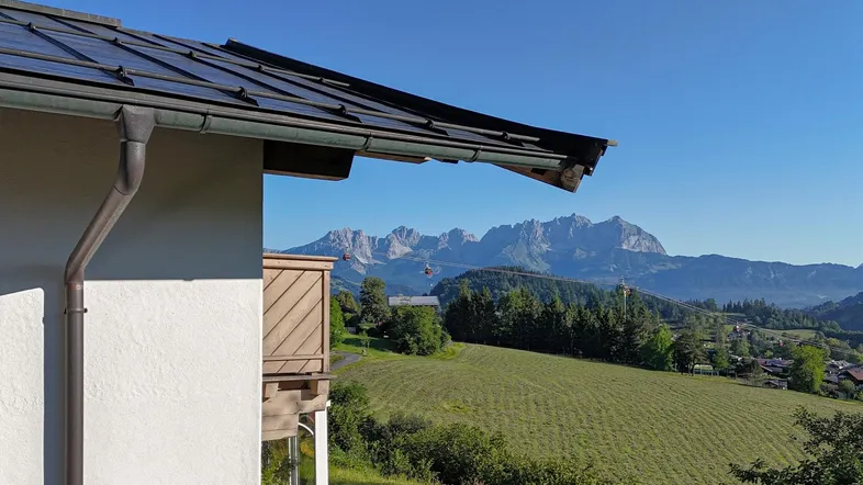 Blick vom Balkon auf die umliegende Berglandschaft mit Solaranlage auf dem Dach.