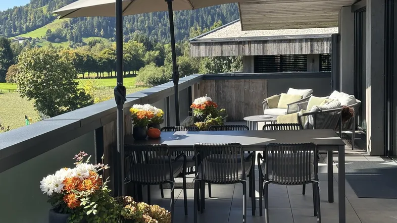Geräumige Terrasse mit Esstisch, Sonnenschirm und Blick auf die umliegende Berglandschaft.