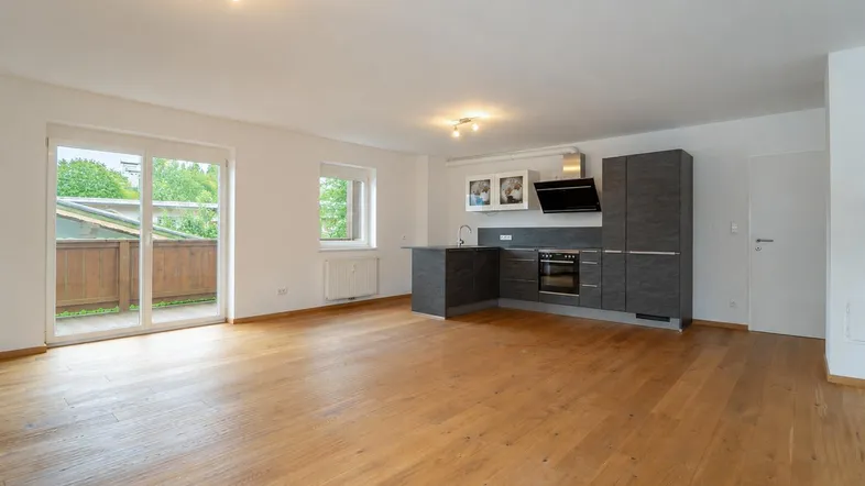 Heller, offener Wohnbereich mit moderner Einbauküche, Holzboden und direktem Zugang zum Balkon.