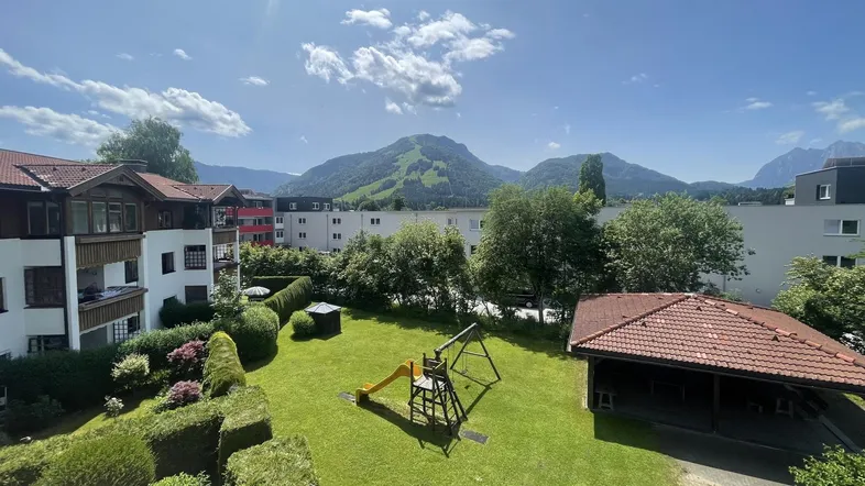 Grüne Gartenanlage mit Spielplatz und beeindruckendem Bergblick in einer Wohnanlage.