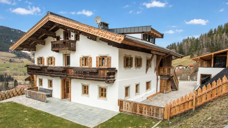 Traditionelles Alpenhaus mit Holzbalkonen und weißer Fassade, umgeben von grüner Landschaft.