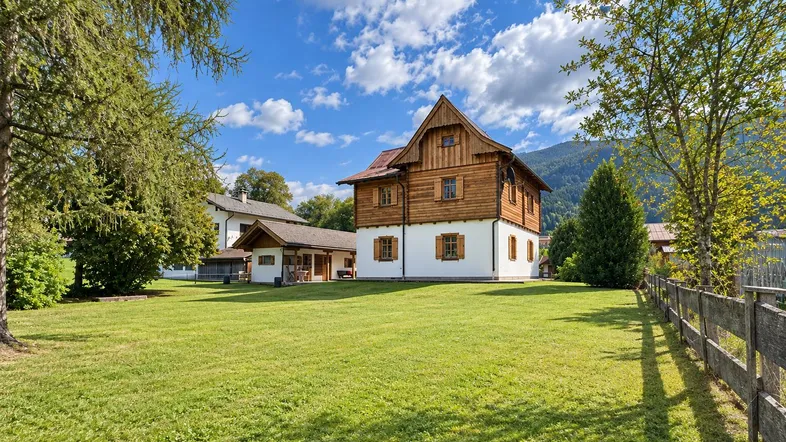 Traditionelles Holzhaus mit großem Garten und Bergblick unter blauem Himmel.