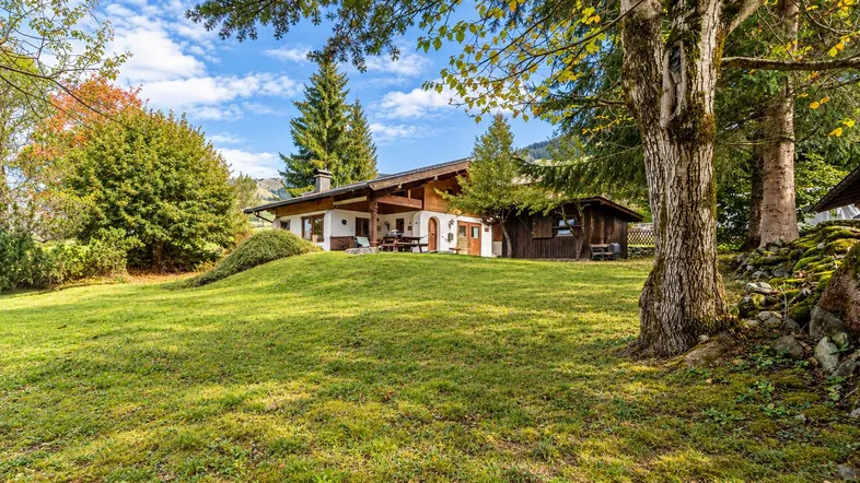 Großzügiger Gartenbereich mit weitläufiger Rasenfläche und traditionellem Landhaus im Hintergrund unter blauem Himmel.