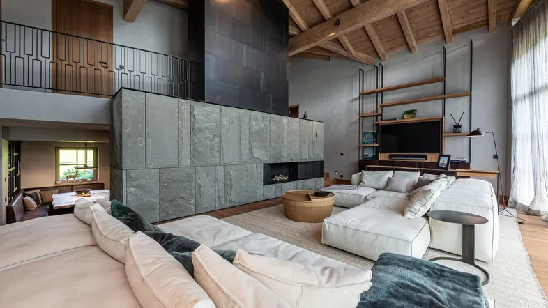 Großzügiges Wohnzimmer mit hohen Holzdecken, modernem Kamin und bequemer Sofalandschaft.