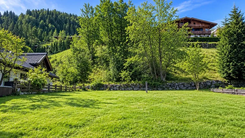 Weitläufige Grünfläche mit Blick auf die umliegende Berglandschaft und traditionelle Häuser.