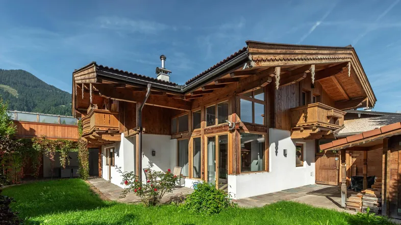 Charmantes Haus im alpinen Stil mit Holzbalkonen, großen Fenstern und gepflegtem Rasen.