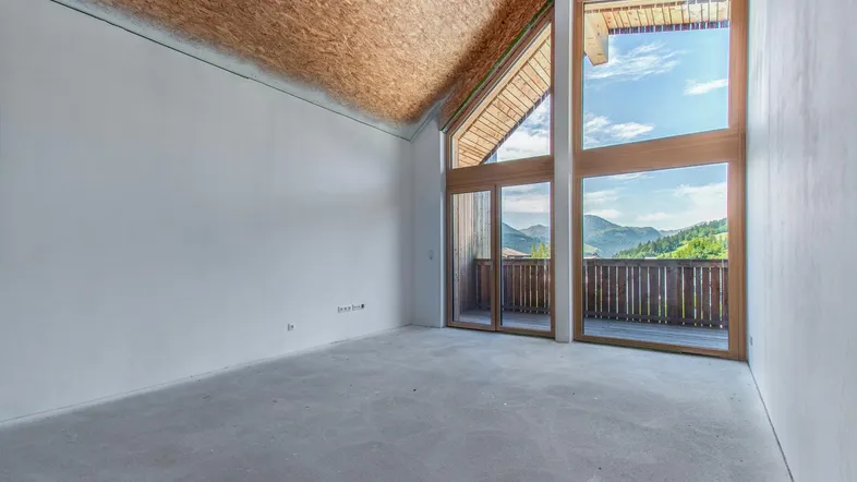 Heller, unfertiger Raum mit hohen Decken, Holzbalken und großen Fenstern mit Bergblick.