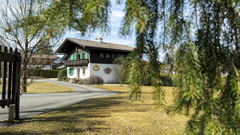 Traditionelles Haus im alpenländischen Stil mit grünen Fensterläden und gepflegtem Vorgarten.