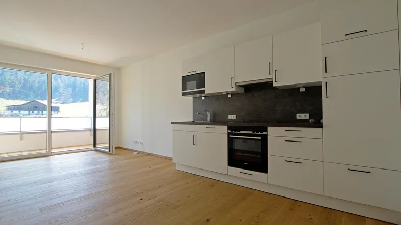 Moderne Küchenzeile in einem hellen Wohnbereich mit Holzboden und Zugang zu einem Balkon mit Bergblick.