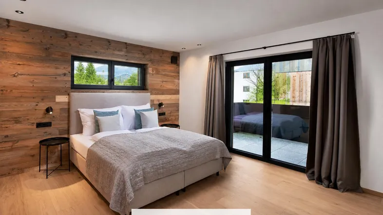 Helles Schlafzimmer mit Holzwand, großem Bett und Zugang zu einem Balkon mit grüner Aussicht.