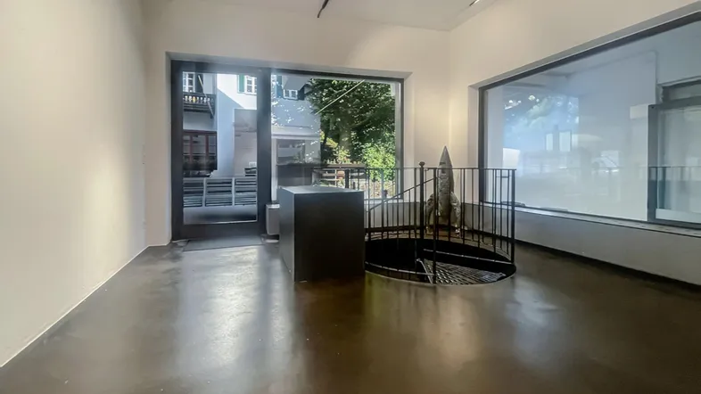 Heller, offener Gewerberaum mit großen Fenstern, Betonboden und einer Wendeltreppe ins Untergeschoss.