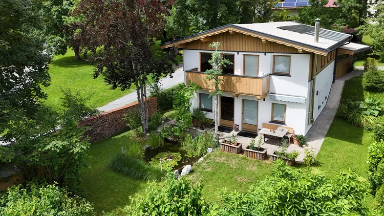 Charmantes Haus mit gepflegtem Garten, kleinem Teich und Balkon, umgeben von üppigem Grün.