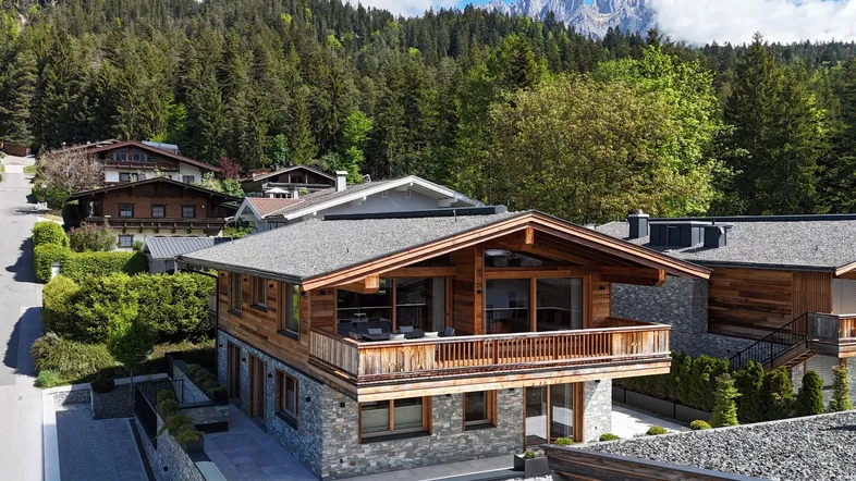 Charmantes Chalet mit Holzfassade und Steinelementen vor einer beeindruckenden Bergkulisse.