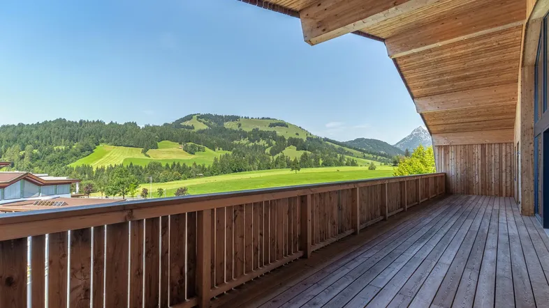 Geräumiger Holzbalkon mit atemberaubendem Blick auf die umliegende grüne Landschaft und die Berge.