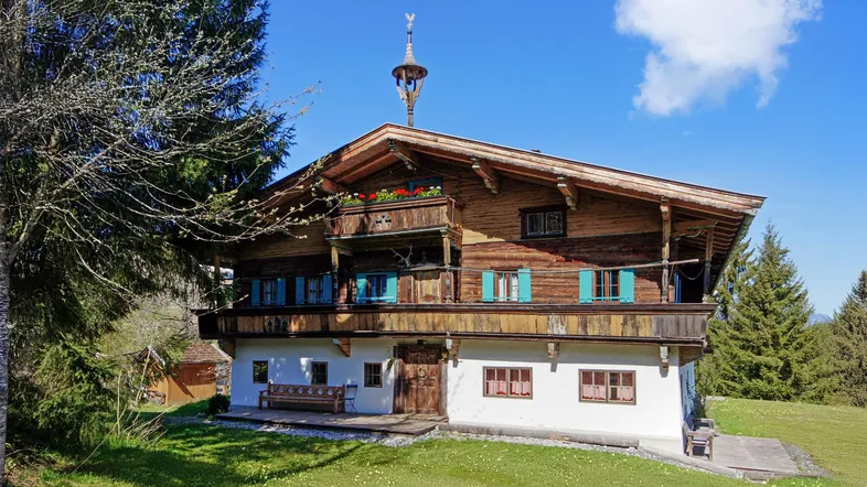 Traditionelles Holzchalet mit Balkonen und Satteldach, umgeben von grünen Wiesen und Bäumen unter blauem Himmel.
