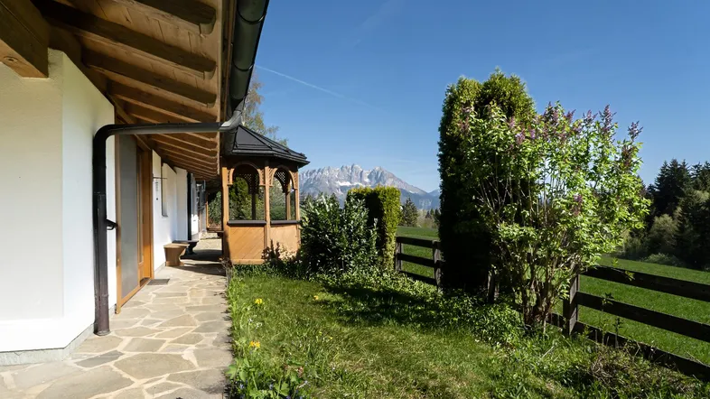 Ein gepflasterter Weg führt entlang des Hauses zu einem kleinen Holzpavillon mit Bergblick.