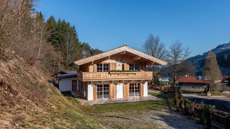 Charmantes Holzchalet mit traditioneller Architektur, umgeben von Natur und Bäumen am Hang.