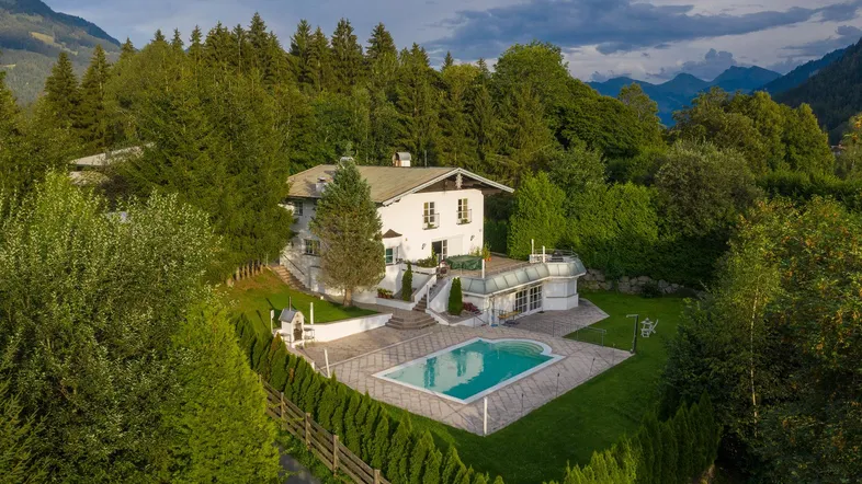 Luftaufnahme eines weißen Hauses mit Pool, umgeben von üppiger grüner Natur und Bergen.