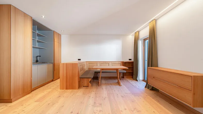 Heller offener Wohn-Essbereich mit Holzboden, integrierter Küchenzeile und Zugang zum Balkon.