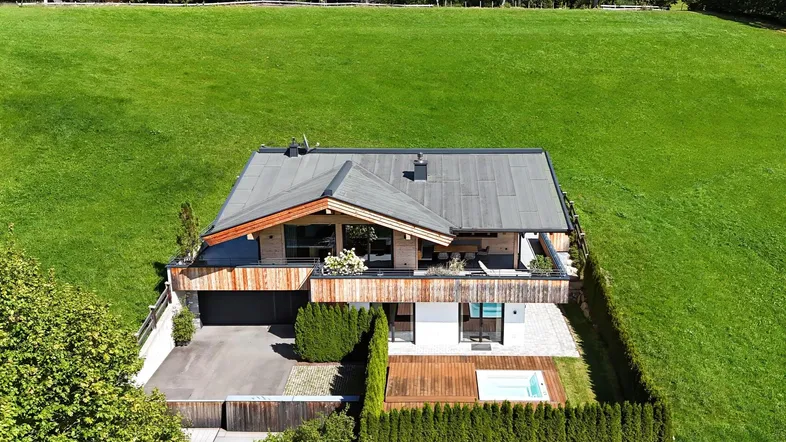 Luftaufnahme eines modernen Chalets mit Holzelementen, umgeben von grünen Wiesen und Bergen.