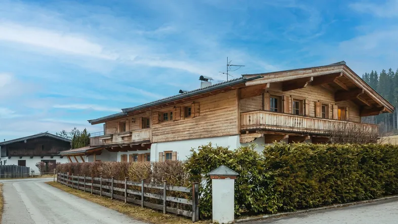 Traditionelles Holzhaus im alpinen Stil mit Balkonen und gepflegter Hecke unter blauem Himmel.