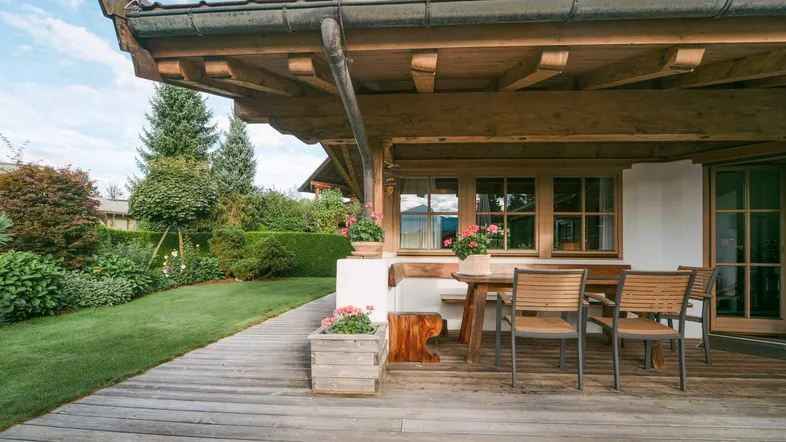 Gemütliche Holzterrasse mit Esstisch und Stühlen, umgeben von gepflegtem Garten und grüner Hecke.
