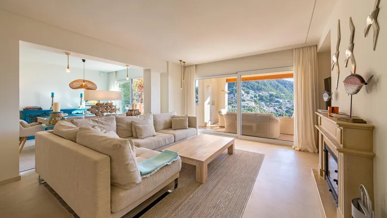 Helles Wohnzimmer mit beigem Sofa, Holztisch und Zugang zu einem Balkon mit Bergblick.