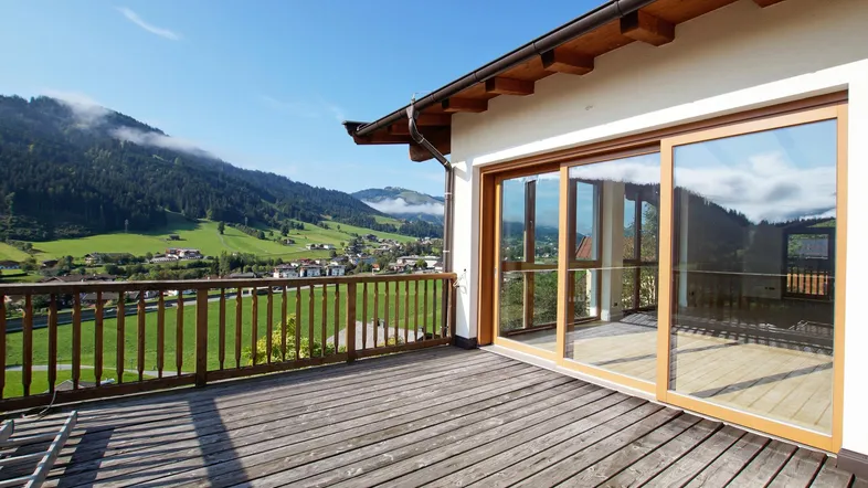 Geräumiger Balkon mit Holzboden und weitem Blick über das Tal und die umliegenden Berge.