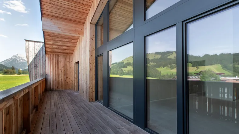 Geräumiger Holzbalkon mit großen Glasfronten und weitem Blick auf die umliegende Berglandschaft.