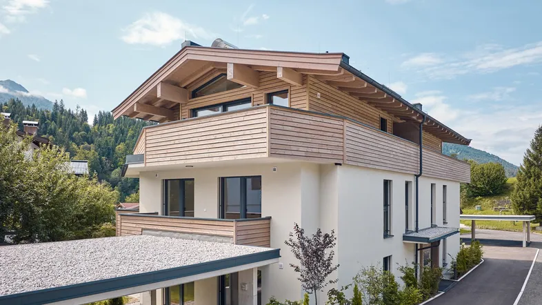 Modernes Mehrfamilienhaus im alpinen Stil mit Holzverkleidung und Carport in den Bergen.
