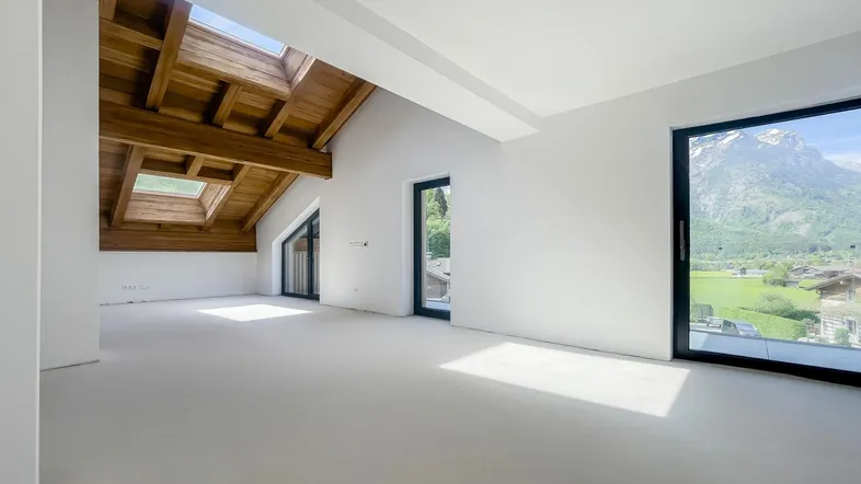 Helles Dachgeschosszimmer mit sichtbaren Holzbalken, großen Fenstern und Bergblick.