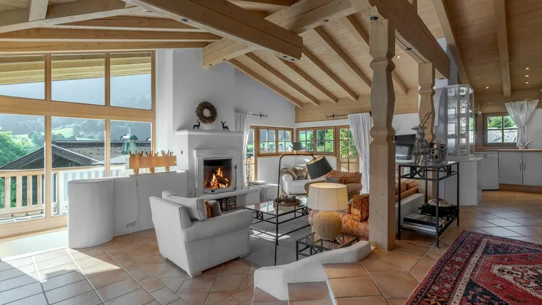 Geräumiges Wohnzimmer mit Kamin, hohen Holzdecken und großen Fenstern mit Bergblick.