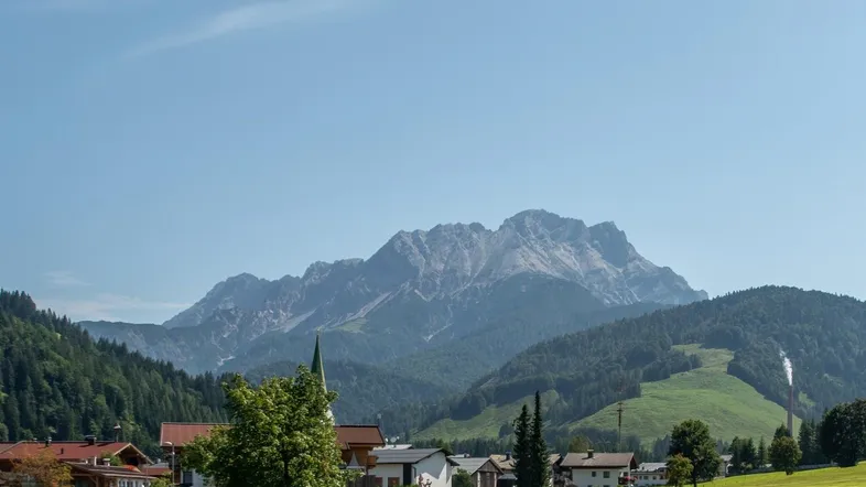 Panoramablick auf ein malerisches Bergdorf mit majestätischen Bergen im Hintergrund unter blauem Himmel.