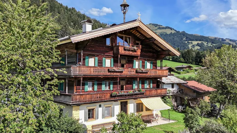 Traditionelles Holzhaus im alpinen Stil mit Balkonen und Bergblick unter blauem Himmel.